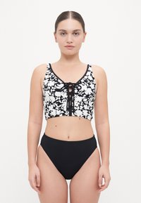Crop top floreale in bianco e nero con una scollatura con lacci, abbinato a un bikini nero a vita alta. Tessuto liscio, design aderente.