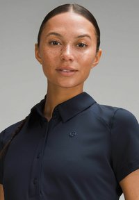 Polo majica tamnoplave boje izrađena od teksturiranog materijala s ovratnikom, s malim logom na lijevoj strani prsnog koša i dugmadima sprijeda.