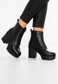 Botines negros de tacón hechos de cuero suave, con un diseño de cordones en la parte delantera, suela de plataforma robusta y textura resistente para un buen agarre.