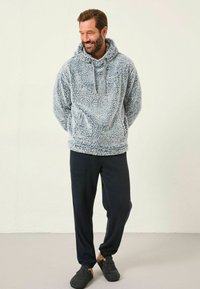 Wuscheliger hellblauer Pullover-Hoodie mit Kängurutasche, kombiniert mit dunklen Hosen und grauen Hausschuhen. Weicher Stoff und lässige Passform.