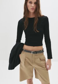 Fekete, hosszú ujjú crop top, amelyet magas derekú khaki sorttal párosítottak, fekete szövegekkel díszített övvel. Texturált anyag és testre szabott fazon.