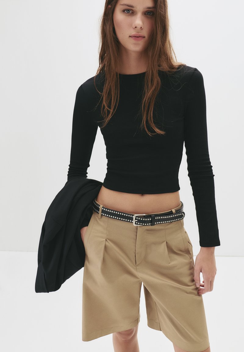 Fekete, hosszú ujjú crop top, amelyet magas derekú khaki sorttal párosítottak, fekete szövegekkel díszített övvel. Texturált anyag és testre szabott fazon.