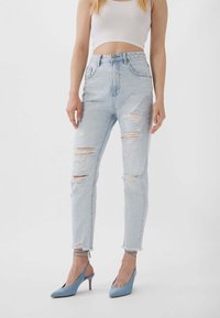 Ljusblå högmidjade jeans med slitna detaljer, fransade fållar och hål; tillsammans med blå spetsiga klackar.