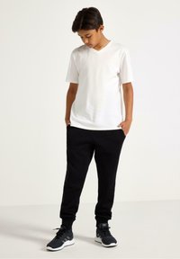 Hvid bomulds t-shirt med V-hals kombineret med sorte sweatpants. Modellen har sorte atletik sko med detaljer på. Enkel og afslappet design.