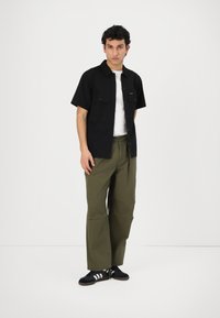 Čierna krátkodrážková košeľa s dvoma prednými vreckami, v kombinácii so zelenými širokými nohavicami a čiernymi topánkami s bielymi pruhmi. Jednofarebný, neformálny dizajn.