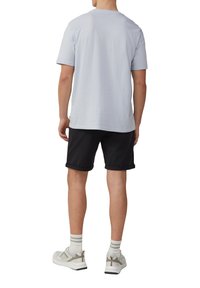 Lichtblauw T-shirt met korte mouwen, zwarte shorts met opgerolde zoom, witte en grijze sneakers met gestructureerde accenten, zichtbare enkelsokken.