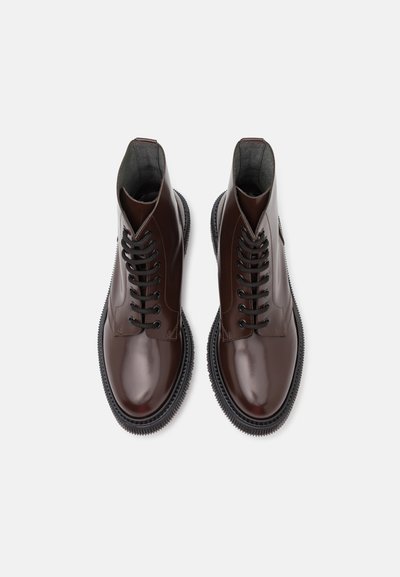 Bottines en cuir marron avec une finition brillante, bout rond, lacets noirs et semelle texturée, comportant un accent cousu autour du bord.