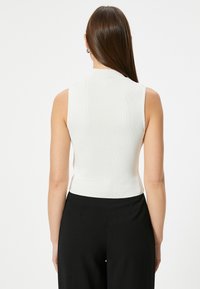 Witte, sans-manche top met een ribbelstructuur en hoge kraag, gecombineerd met zwarte, hoge taille broeken. Eenvoudig en aansluitend ontwerp.