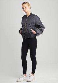 Black bomber jacket with a zip front, knit collar, and side pockets, paired with black leggings and white sneakers on a gray background.