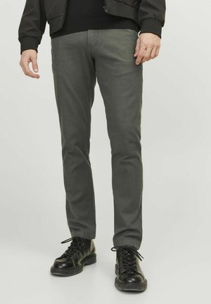 Dunkelgraue, schmal geschnittene Hosen aus einem strukturierten Stoff. Verfügen über ein klassisches Fünf-Taschen-Design und werden mit schwarzen Schnürstiefeln getragen.