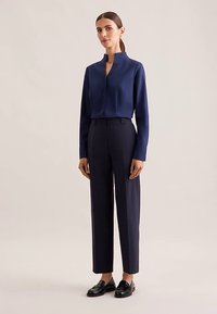 Navy blue long-sleeve shirt with a stand-up collar and two chest pockets, paired with high-waisted tailored trousers and black loafers.