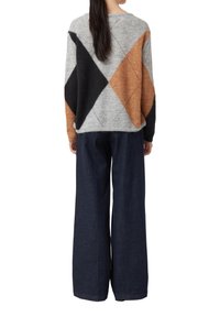 Grauer Strickpullover mit schwarzen, oranges und hellgrauen Rautenmuster, kombiniert mit weit geschnittenen, dunklen Jeans. Weiche Textur und lässige Passform.