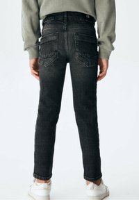 Vaqueros de mezclilla negra de pierna recta, con bolsillos traseros y detalles de costura sutiles. Combinados con un suéter gris y zapatos blancos.