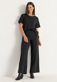 Zwarte top en wijde broek gemaakt van een gladde, rekbare stof. Heeft een relaxte pasvorm, korte mouwen en zijnaaddetails.