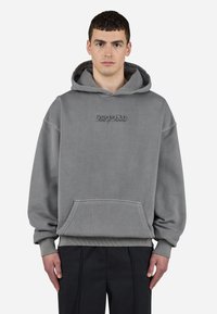 Sudadera gris de gran tamaño con un bolsillo canguro, puños de canalé y capucha con cordón. Presenta texto bordado en el pecho.