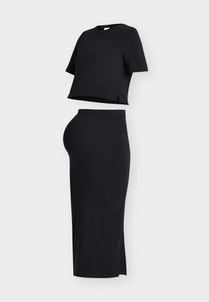 Czarny dwuczęściowy strój z krótkim, krótkim topem i dopasowaną spódnicą midi z wysokim stanem i rozcięciem z boku na białym tle.