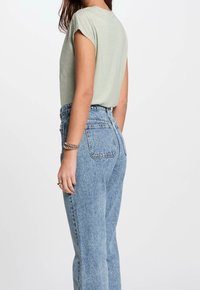 Jasnozielona bluzka z krótkim rękawem w luźnym kroju, zestawiona z niebieskimi dżinsami o wysokim stanie z teksturowanym wykończeniem i dwoma tylnymi kieszeniami.