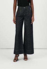 Dunkelblaue weite Jeans mit hoher Taille, ausgestattet mit zwei Fronttaschen und kontrastierendem gelben Nähten. Der Stoff hat eine glatte Textur.