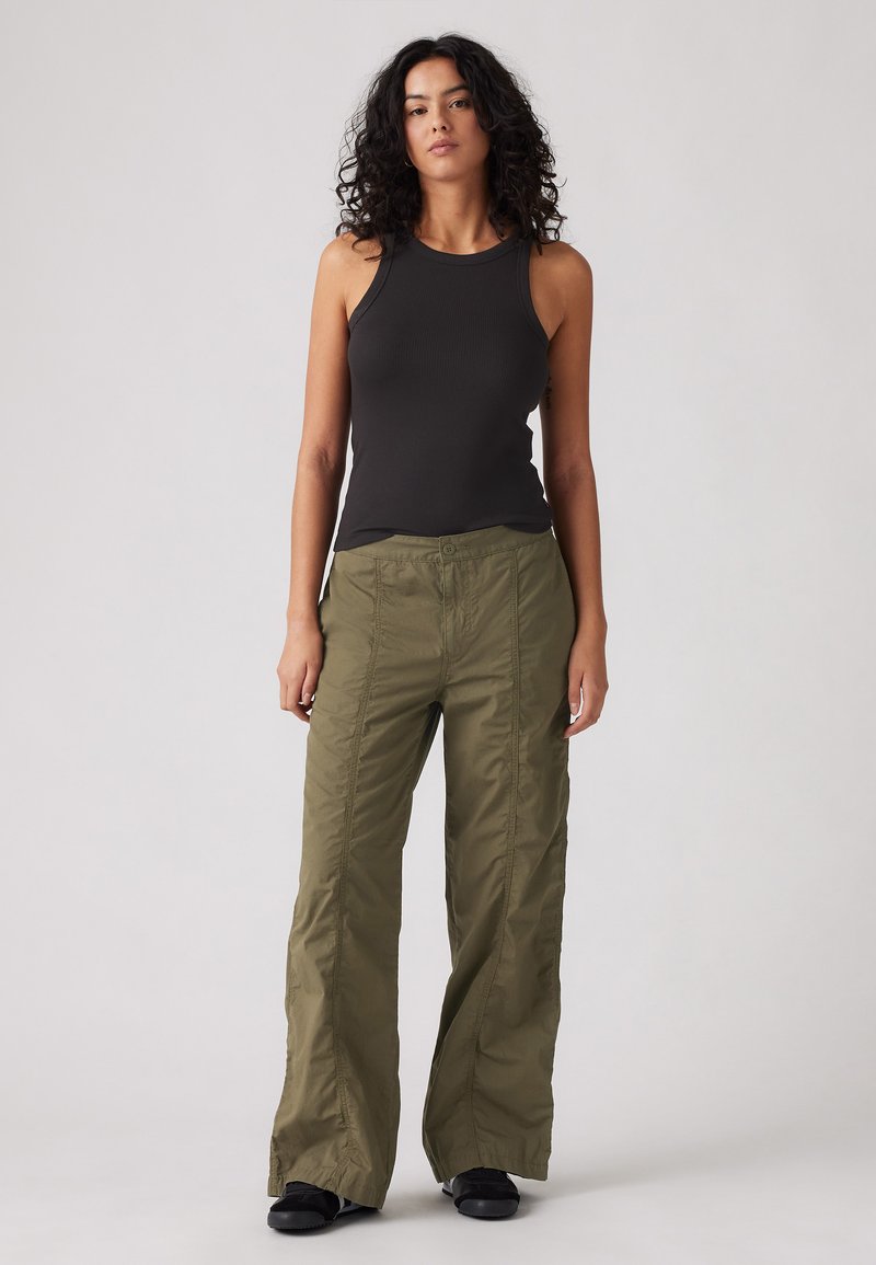 Débardeur noir à côtes associé à un pantalon large vert olive avec des détails de couture à l'avant et une fermeture à bouton.