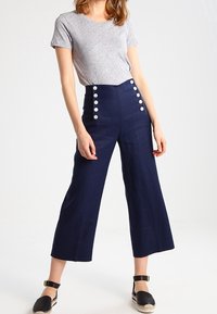 Graues T-Shirt mit kurzen Ärmeln, kombiniert mit hochtaillierten marineblauen Culottes, die große weiße Knöpfe an der Seite haben, und schwarzen Espadrilles.