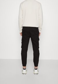 Svarta cargobyxor i bomull, med slim fit, flera fickor och elastiska muddar, ihop med vita sneakers.