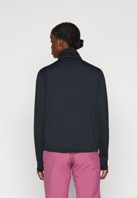 Sort langærmet top med høj krave, tekstureret design og en afslappet pasform, parret med lyserøde bukser. Stoffet ser glat og holdbart ud.