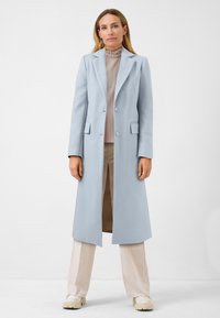 Lichtblauwe lange jas met een op maat gemaakte ontwerp, met notch-lapels, twee knopen en zijzakken, gedragen over een geplooide crèmekleurige top en beige broek.