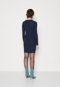 Robe en tricot côtelé bleu marine à manches longues et à silhouette ajustée, associée à des bottines à talons bleu clair, vue de dos.