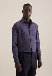 Camicia a bottoni viola con motivo geometrico, con colletto a punta e maniche lunghe, abbinata a pantaloni scuri.
