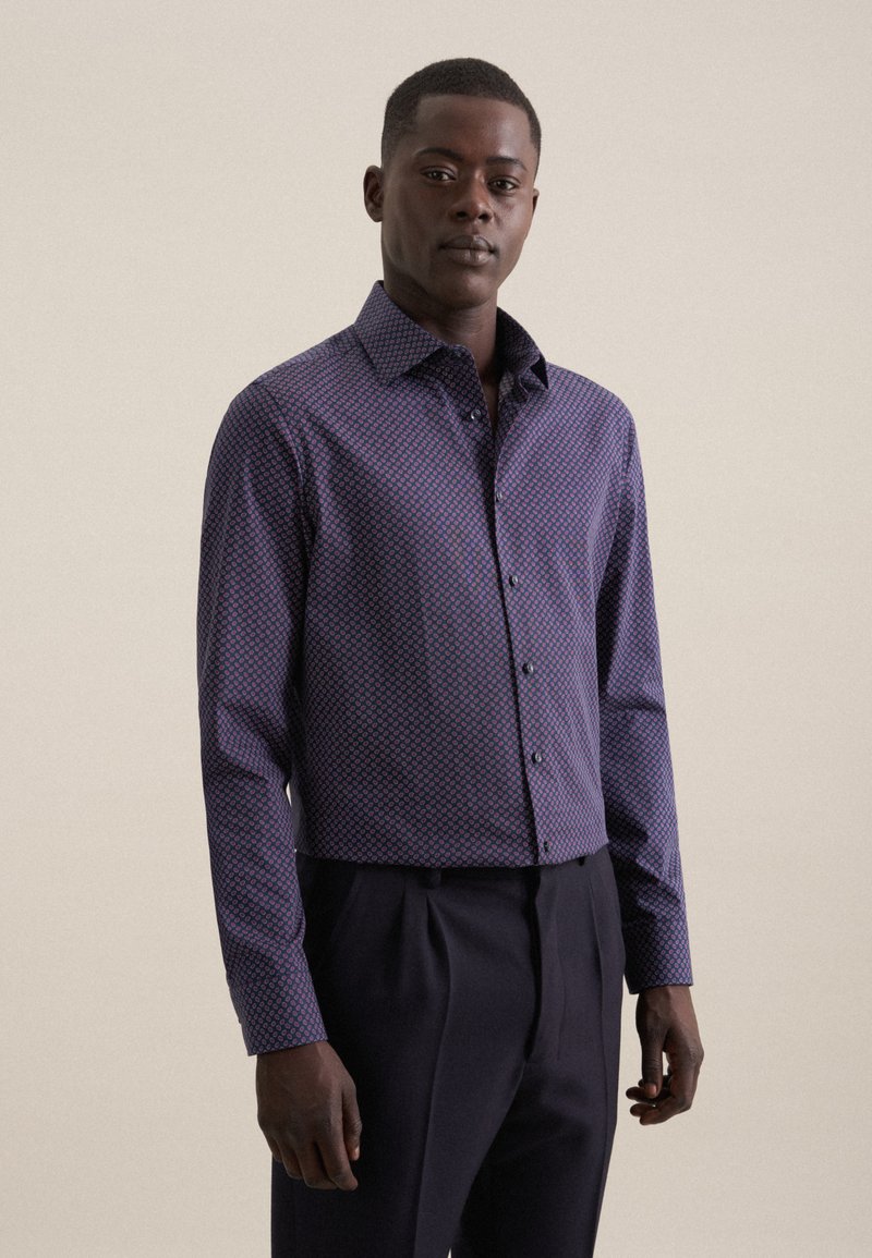 Camicia a bottoni viola con motivo geometrico, con colletto a punta e maniche lunghe, abbinata a pantaloni scuri.