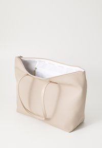 Sac fourre-tout beige en matériau texturé avec une fermeture zippée et deux longues anses, doté d'un intérieur blanc avec une poche zippée.