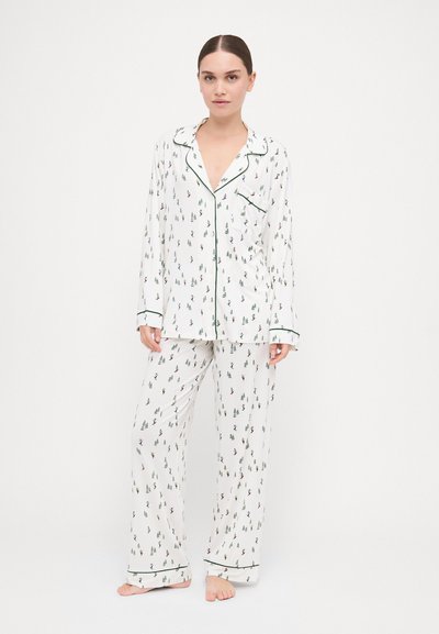 Λευκή πιτζάμα με σχέδιο φυλλώματος, με μακριά μανίκια, πράσινη επένδυση και χαλαρή εφαρμογή. Το υλικό φαίνεται απαλό και ελαφρύ.