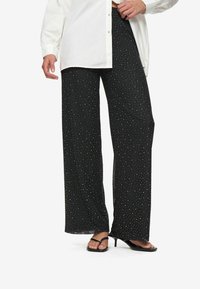 Black wide-leg pants with white polka dots, made from soft fabric. Features a loose fit and pair well with a white shirt.