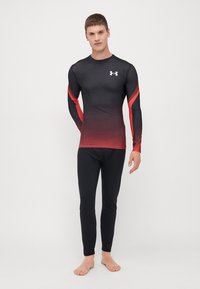 Rash guard noir à manches longues avec des accents dégradés rouges, fabriqué en tissu extensible. Assorti à des leggings noirs, adapté aux activités sportives.