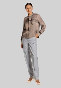 Zijde taupe blouse met strik en knoopsluiting, gecombineerd met lichtgrijze op maat gemaakte broeken en beige hoge hakken.
