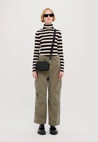 Pulover în dungi negre și crem cu gât înalt, pantaloni cargo largi kaki cu nasturi pe lateral, geantă crossbody neagră și încălțăminte groasă neagră.