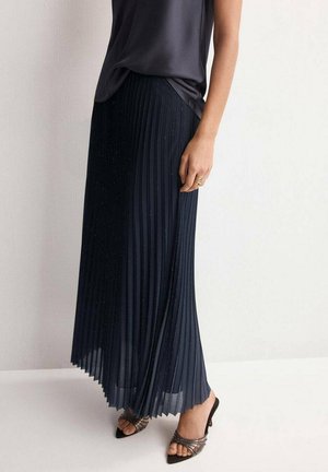 Camisola de satén azul marino con tirantes finos combinada con una falda plisada azul marino con un sutil brillo, llevada con tacones de tiras.