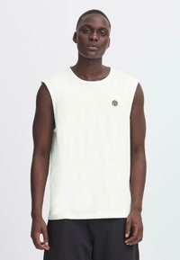 Canotta bianca in cotone senza maniche con collo tondo e piccolo logo geometrico nero sul lato sinistro del petto, abbinata a pantaloni corti scuri.