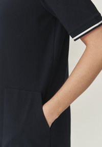 Robe en coton marine avec des manches courtes bordées de blanc, une poche latérale et une silhouette ajustée. Texture douce, design minimaliste.