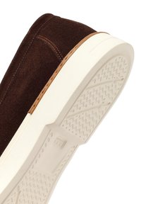 Bruine suède instapper met witte rubberen zool die het geprofileerde loopvlak aan de onderkant toont.