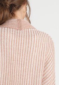Dzianinowy kardigan w delikatnym różu, z prążkowaną fakturą i białymi akcentami. Tył zdobi subtelny wzór jodełki oraz zaokrąglony kołnierz.