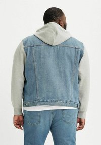 Chaleco de denim en azul claro con un sudadera con capucha gris debajo. Cuenta con costuras clásicas y un ajuste relajado. La vista trasera muestra los bolsillos.