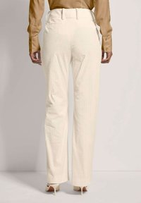 Witte geribbelde broeken met een hoge taille, voorzien van zijzakken en een rechte pijpdesign, gecombineerd met een lichtbruin blouse met lange mouwen.