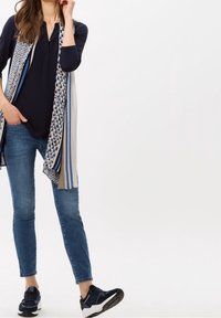 Haut bleu marine avec un décolleté en V, écharpe légère multicolore à rayures, jean bleu et baskets sombres avec une semelle blanche.