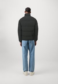 Matte sort pufferjakke med høj krave, udstyret med horisontale syninger og ribbede manchetter, parret med let blå jeans i afslappet pasform.