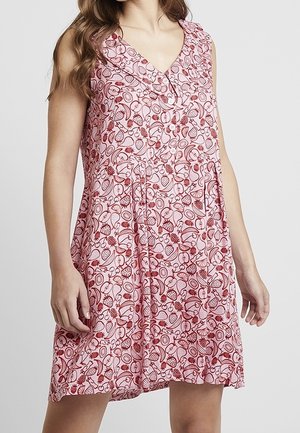Robe rose sans manches avec un motif de fruits rouge et blanc, coupe ample, décolleté en V, portée par une personne debout aux longs cheveux.
