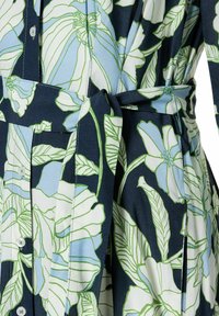 Blumenkleid mit großen weißen und blauen Blumen sowie grünen Blättern auf einem marineblauen Hintergrund, aus leichtem Stoff mit einem Bindegürtel.