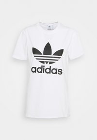 Balta kokvilnas T-kreklā ir liels melns Adidas logo un trīs horizontālas svītras zem logo. Īsās piedurknes un apaļa kakla izgriezuma dizains.