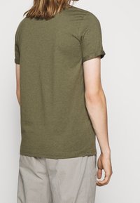 T-shirt verde oliva, a manica corta, con colletto girocollo e maniche arrotolate; realizzato in un morbido tessuto misto cotone con una texture liscia.