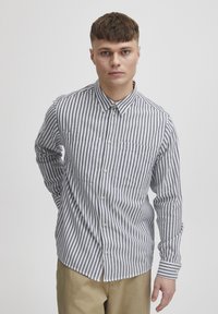 Camicia a righe in bianco e blu navy. Presenta un collo a camicia, due tasche sul petto e maniche lunghe. Realizzata in tessuto leggero.